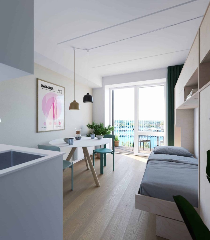 Lys og moderne sydporten lejlighed med åbent opholdsrum, spiseplads, soveområde, stilrent køkken og store vinduer med udsigt mod vand og grønne omgivelser.
