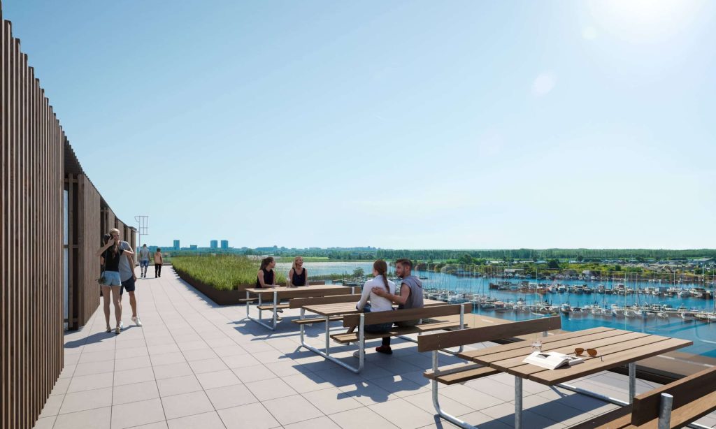 Fælles sydporten tagterrasse med borde og bænke, beboere i ophold og imponerende udsigt over marina, vand og grønne omgivelser på en solrig dag.