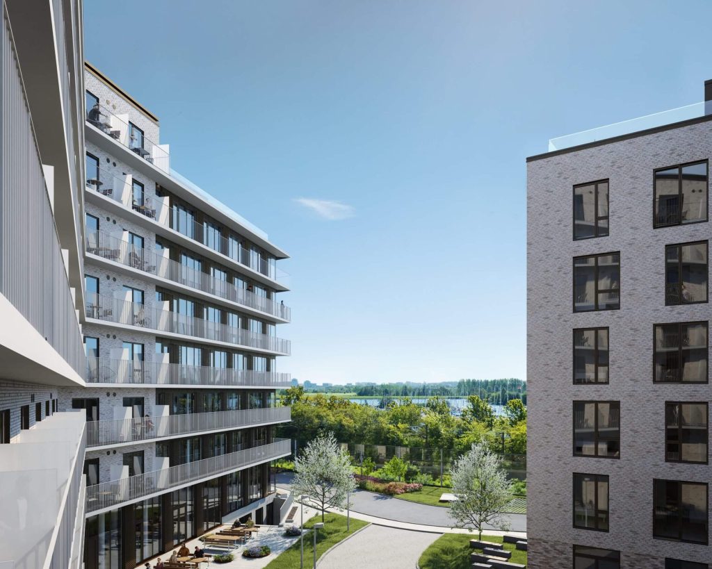 Moderne boligområde med sydporten udsigt over grønne fællesarealer, elegante lejlighedsbygninger med altaner og udsyn mod vand og natur i dagslys.